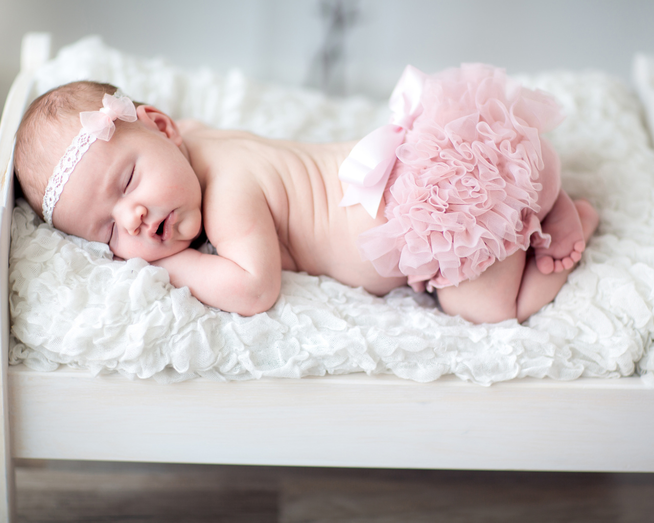 Маленькая спящая девочка в розовом костюме в кроватке