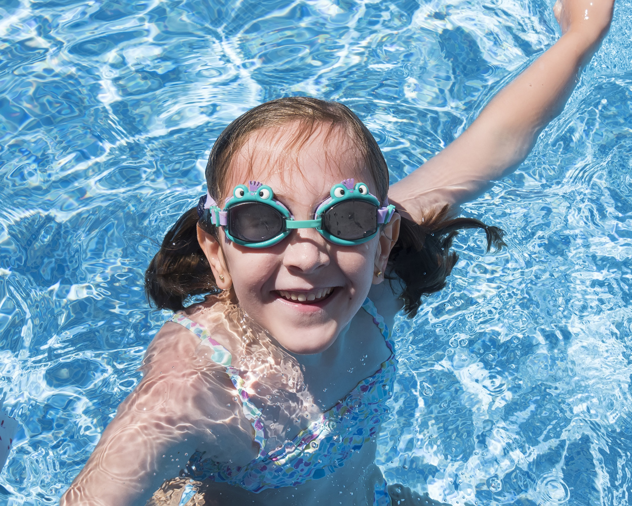 Маленькая улыбающаяся девочка в очках в бассейне 
