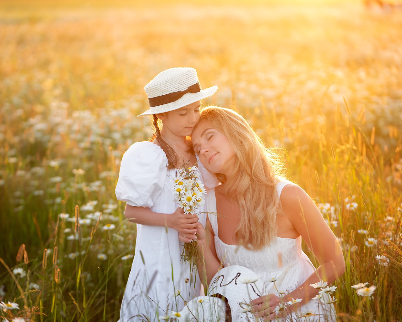 Мать с дочерью на поле с белыми ромашками в лучах солнца 