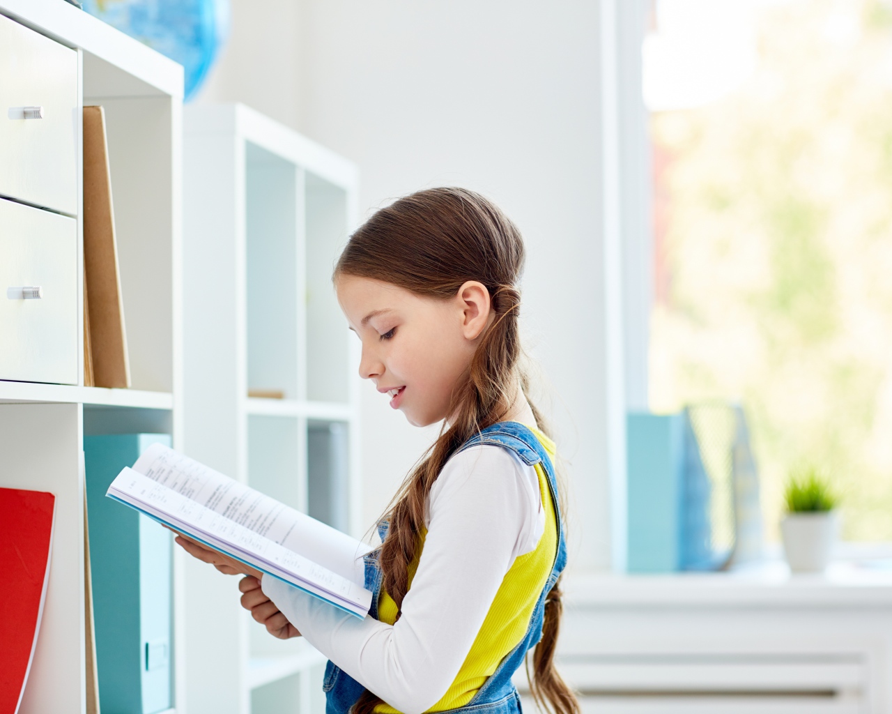 Умная девочка школьница с книгой в библиотеке 