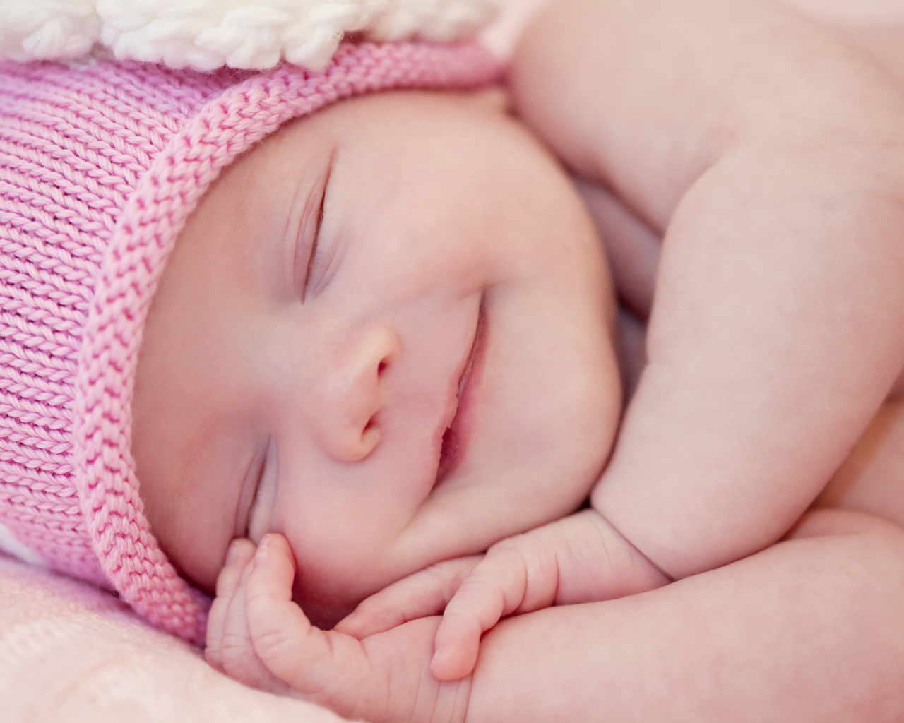 Улыбающийся грудной ребенок в розовой вязаной шапке 