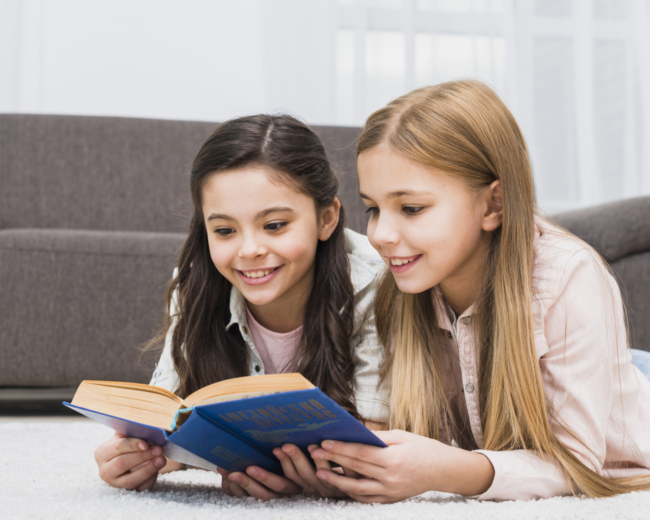 Две маленькие девочки читают книгу на полу