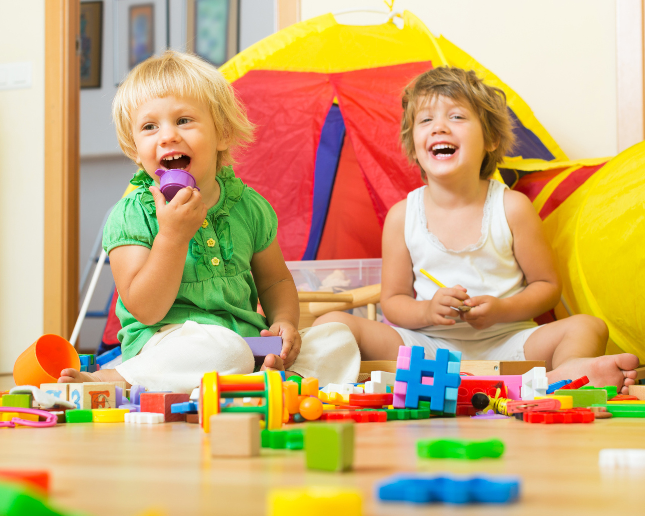 Два улыбающихся ребенка играют с конструктором 