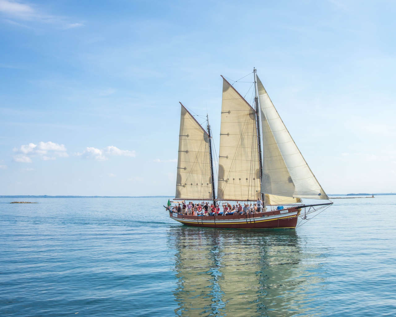 Судно с белыми парусами в море на фоне голубого неба 