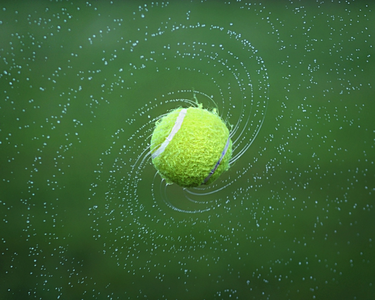 Tennis ball in splashing water on green background