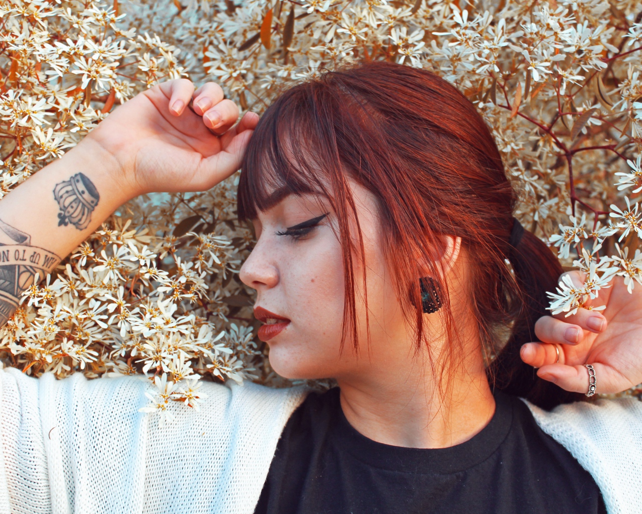 Молодая девушка с татуировкой на руке стоит у цветущего дерева