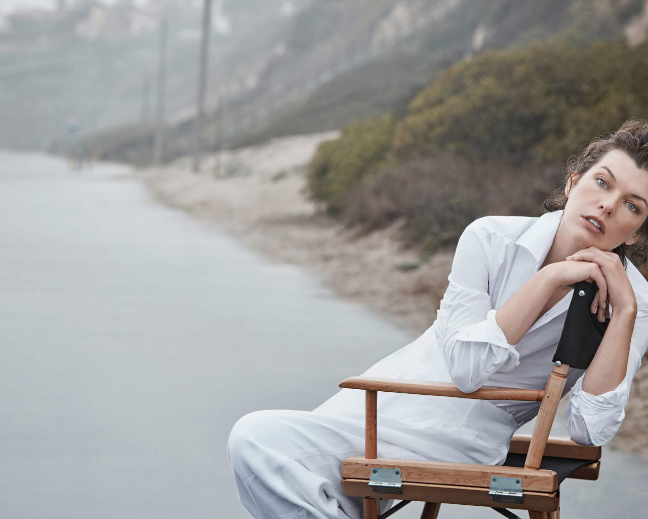 Актриса Милла Йовович в белом платье сидит на стуле