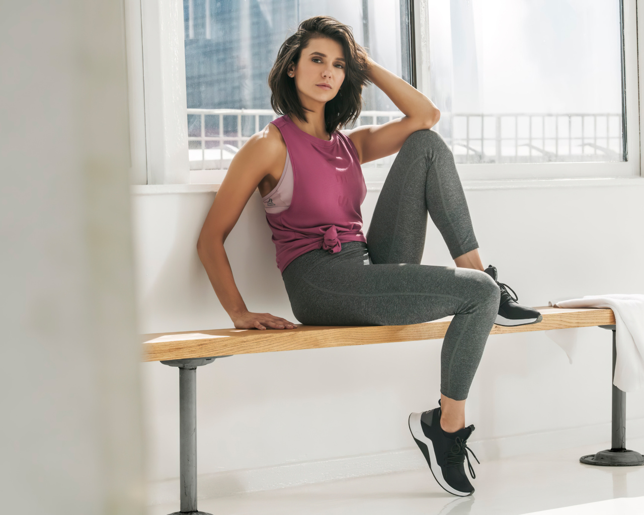 Актриса Нина Добрев сидит на лавке в спортивном костюме