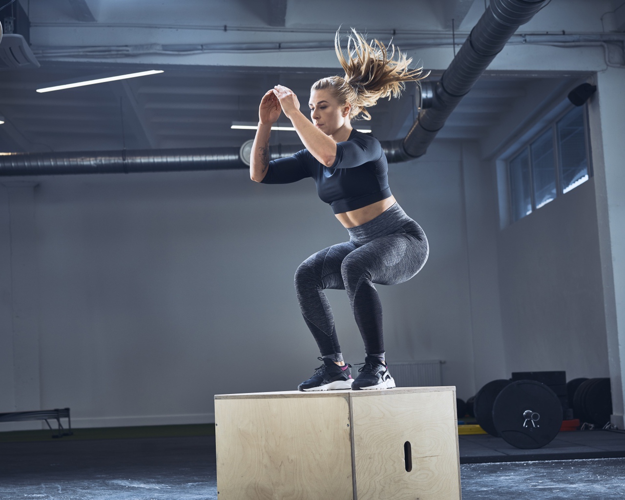 Спортивная девушка запрыгивает на тумбу в спортзале 