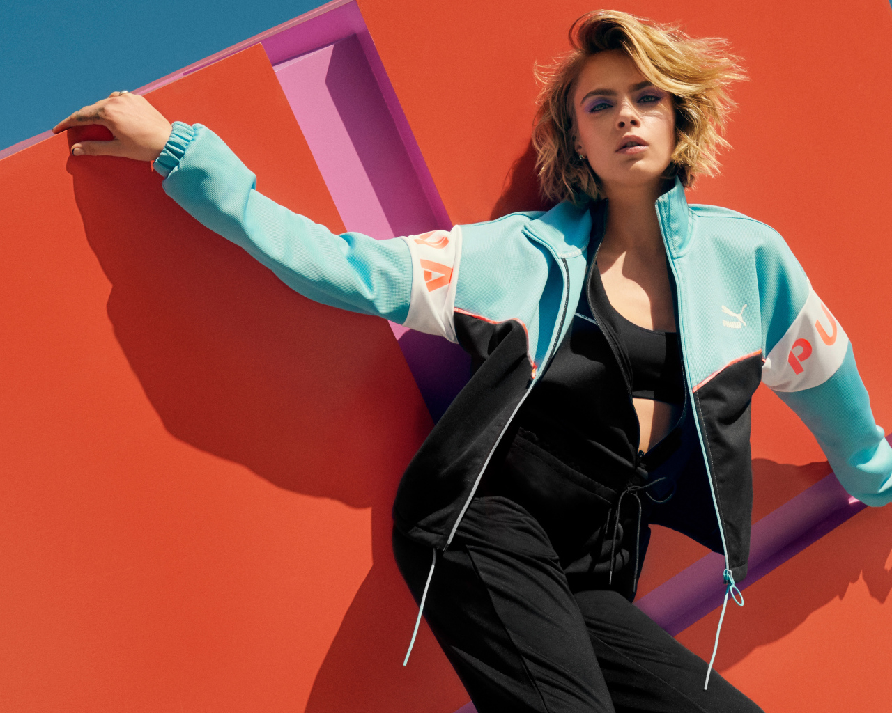 Красивая актриса Кара Делевинь в спортивном костюме у стены 