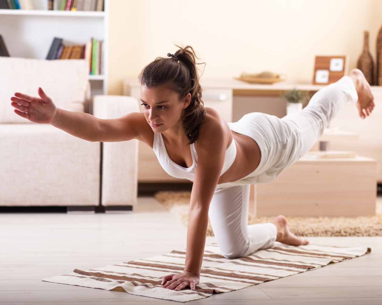 Красивая девушка в белом костюме занимается фитнесом дома