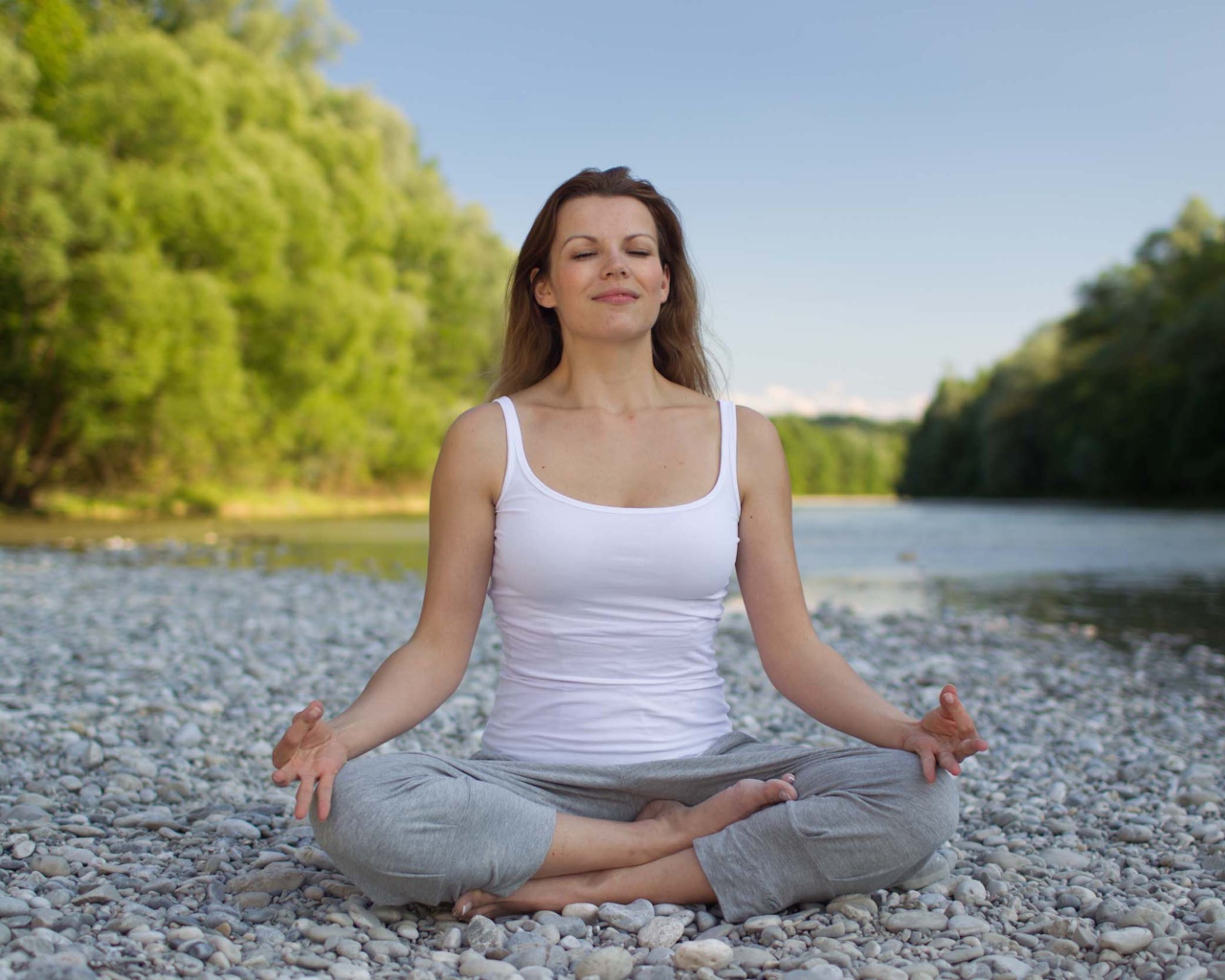 Девушка в позе лотоса медитирует у реки 