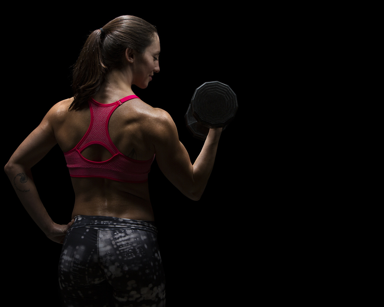 Девушка качает руки гантелей на черном фоне 