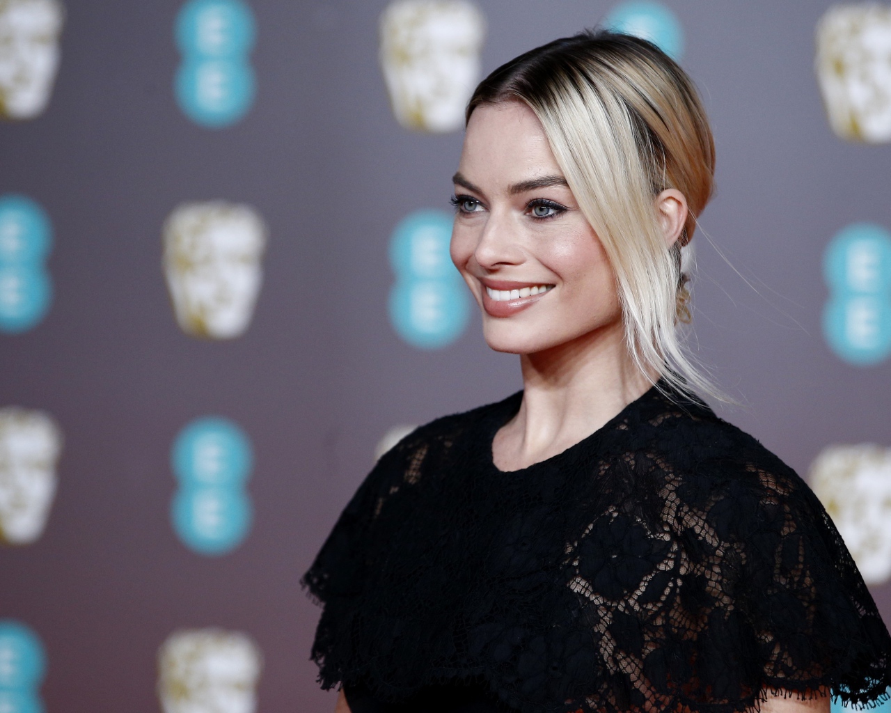 Улыбающаяся актриса Марго Робби в черном платье 