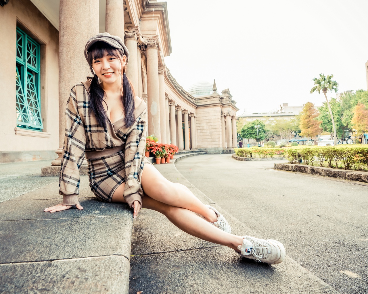 Улыбающаяся азиатка в кепке сидит на ступеньках 