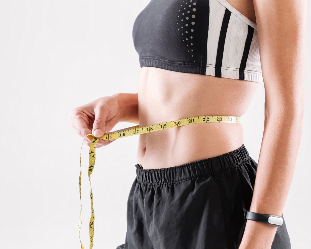 Спортивная девушка меряет талию сантиметром 