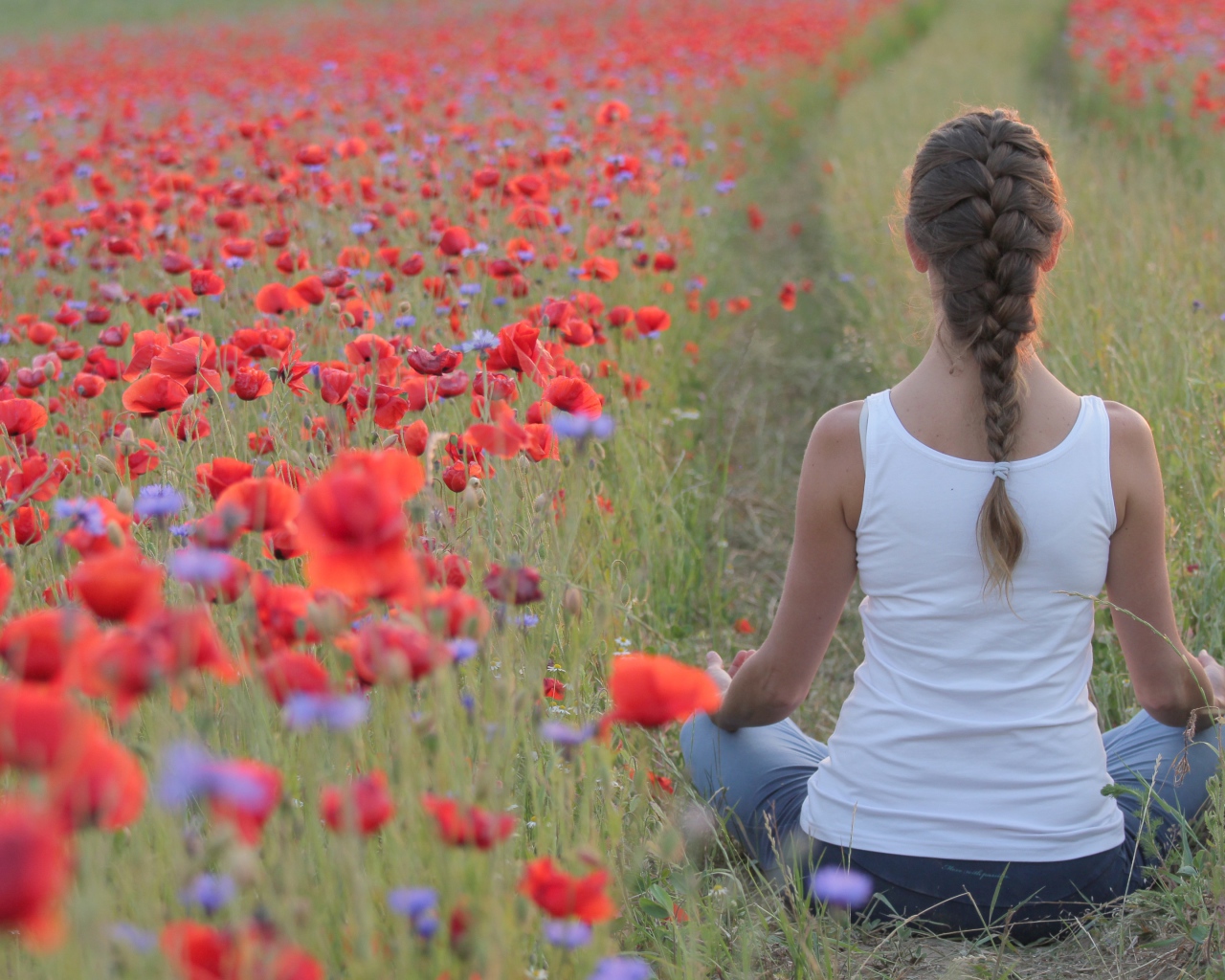 Молодая девушка медитирует на поле с красными маками