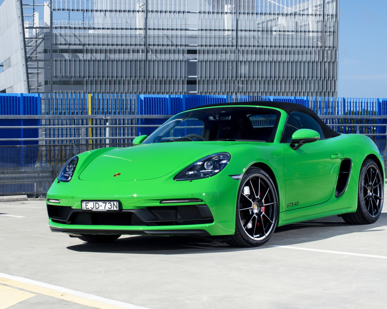 Зеленый автомобиль Porsche 718 Boxster GTS у здания 