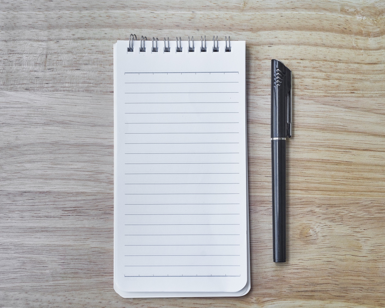 Авторучка и блокнот лежат на деревянном столе