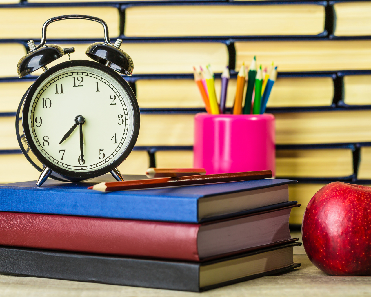 Будильник, книги, карандаши и яблоко на столе у стены 