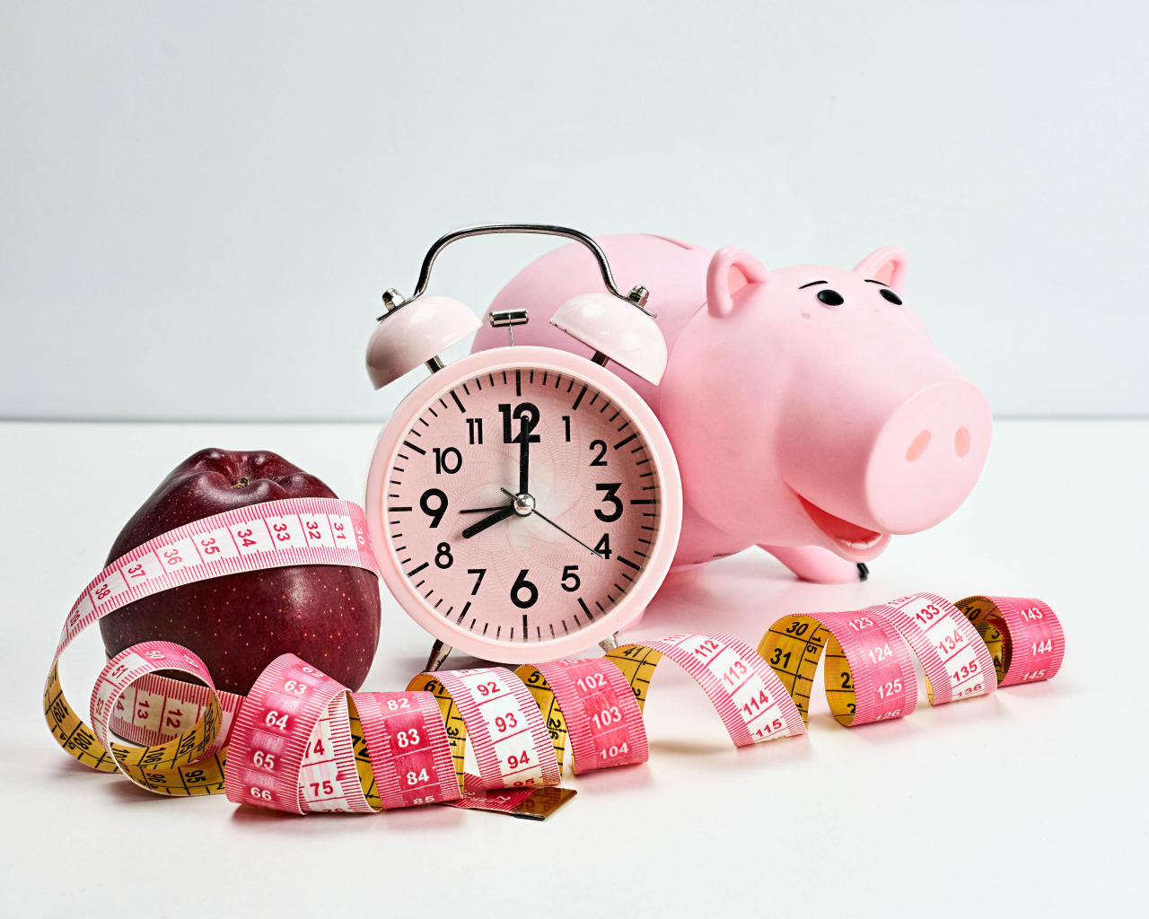 Будильник, свинья копилка, яблоко и сантиметр на белом фоне