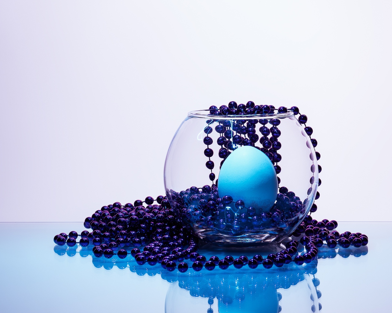 Синие бусы на столе со стеклянной вазой и яйцом