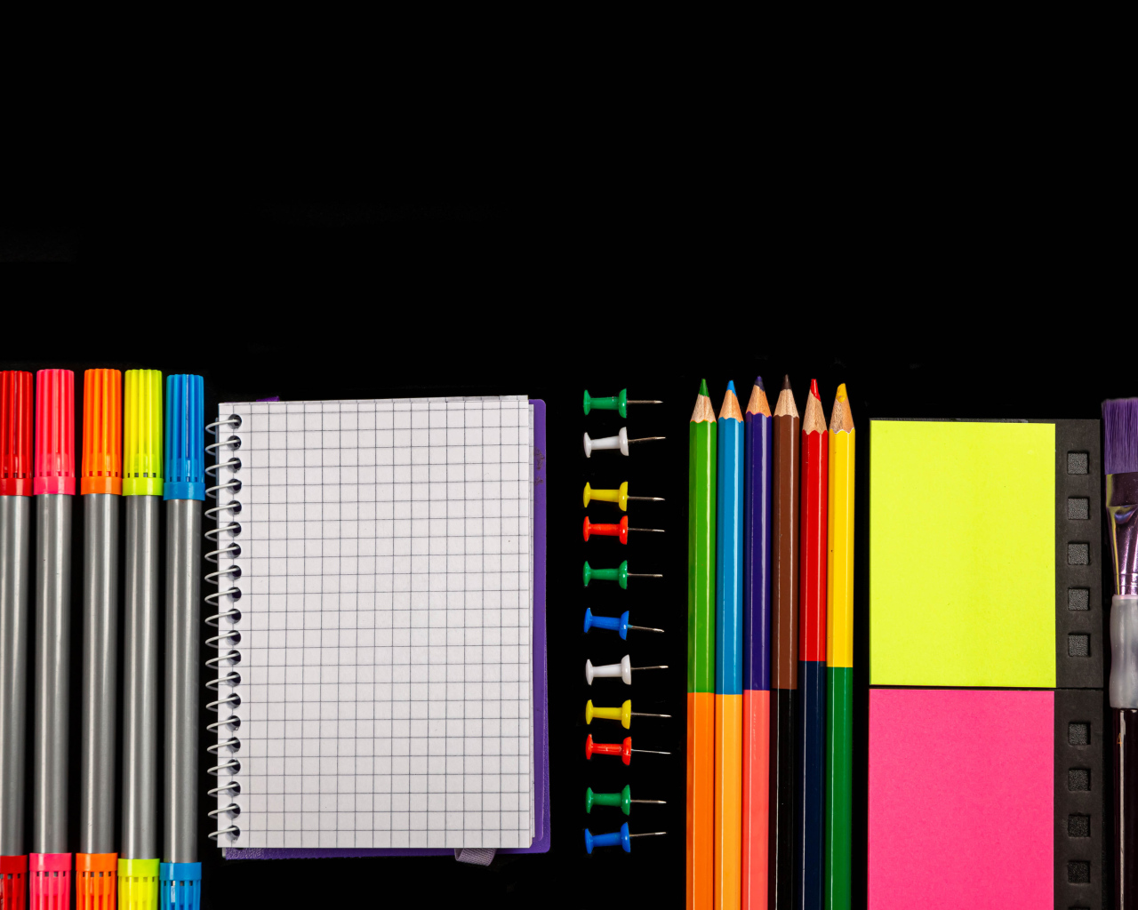 Фломастеры, карандаши, тетрадь и кисточки на черном фоне 