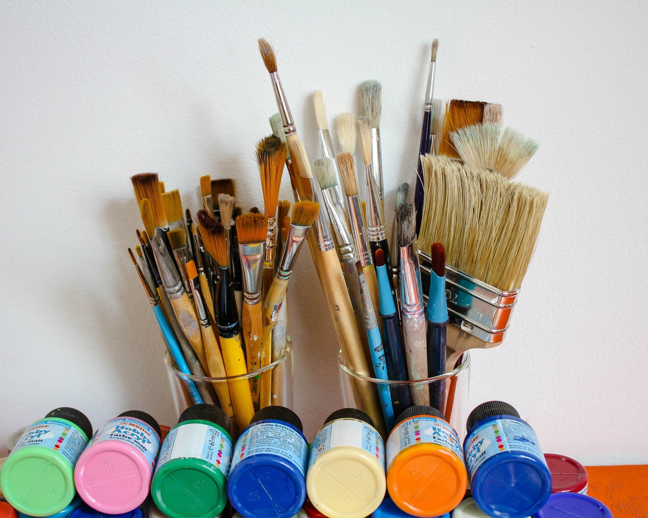 Много кисточек и разноцветные краски у стены