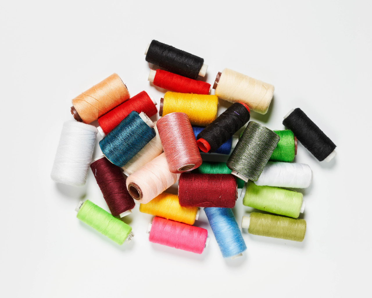 Много катушек разноцветных ниток на белом фоне 
