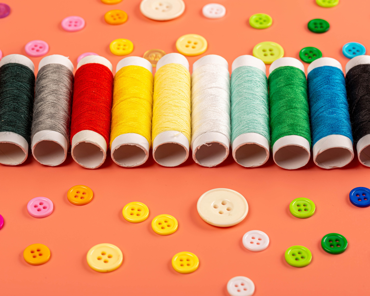 Разноцветные нитки и пуговицы на розовом фоне