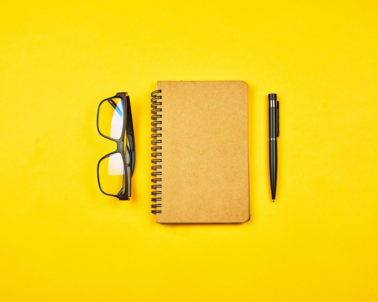 Блокнот, очки и ручка на желтом фоне