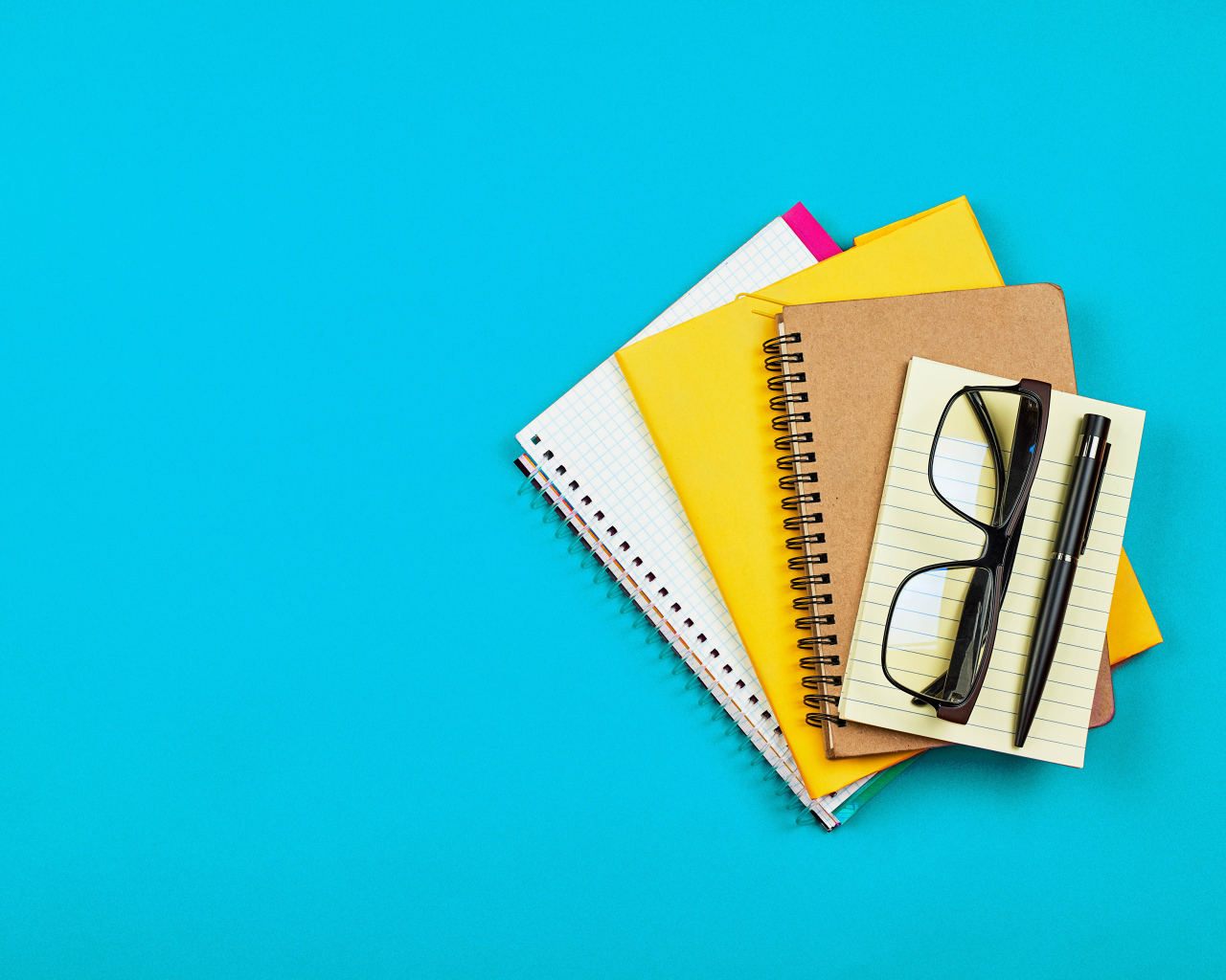 Блокноты, очки и ручка на голубом фоне