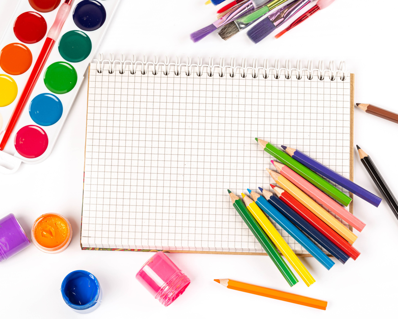Карандаши, краски и тетрадь на белом фоне 