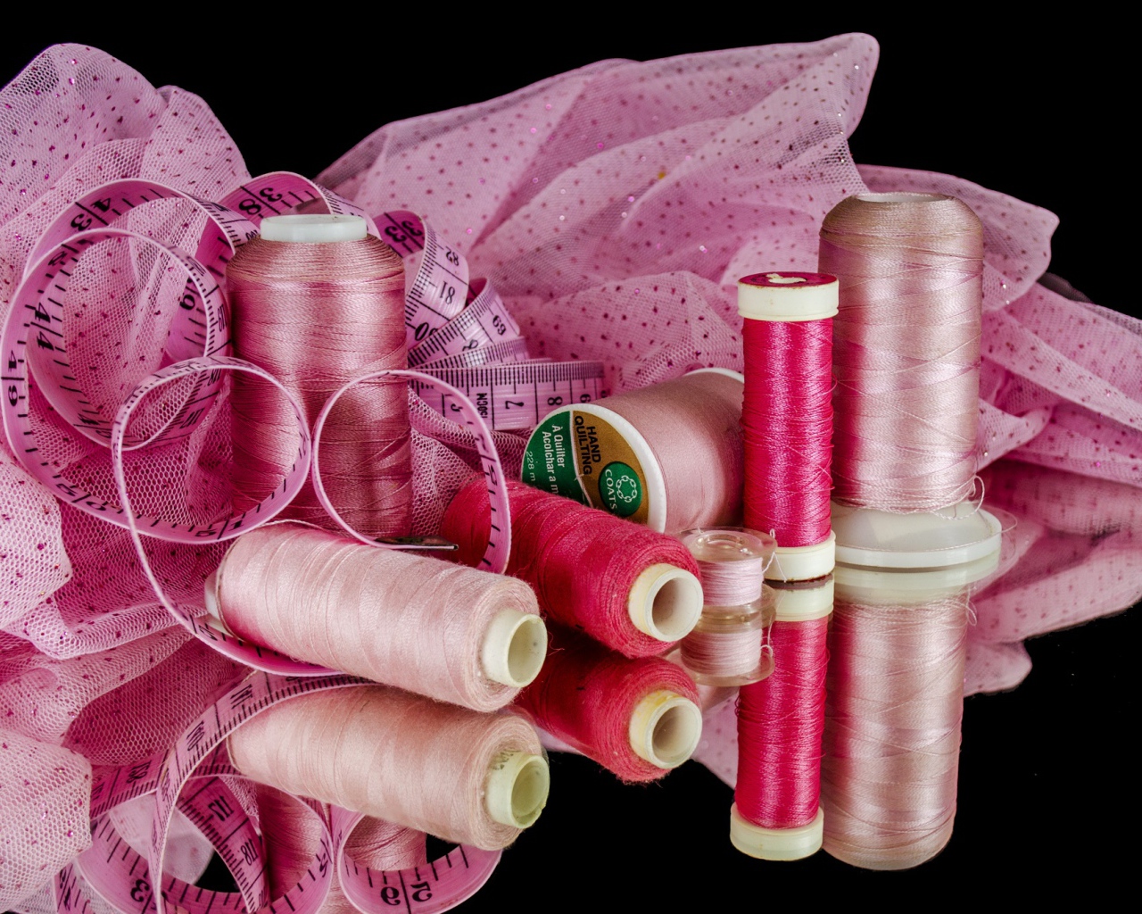 Розовые нитки с сантиметром и тканью на черном фоне 