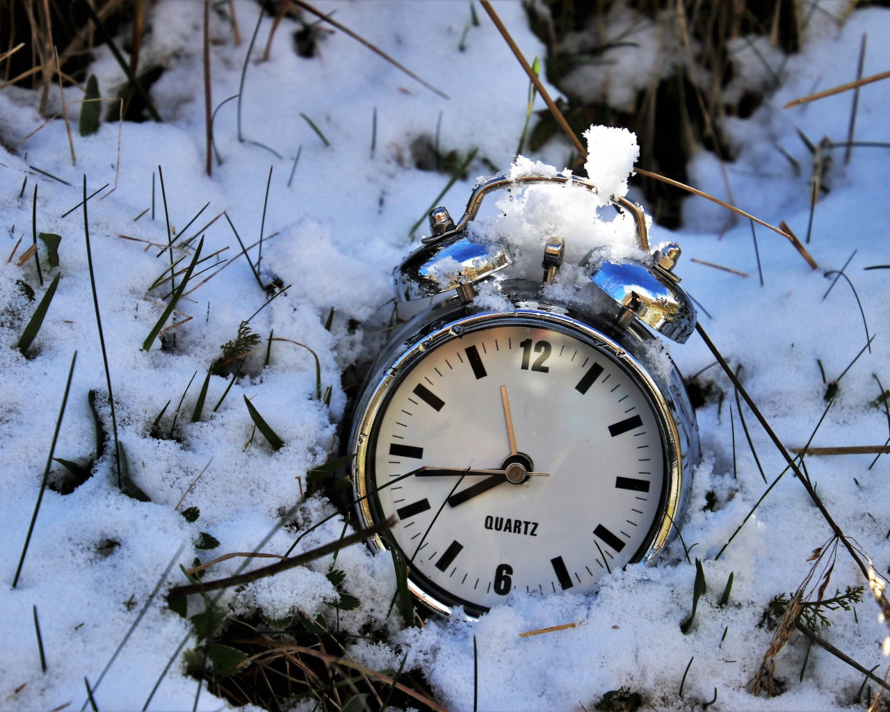 Серебряный будильник лежит в снегу