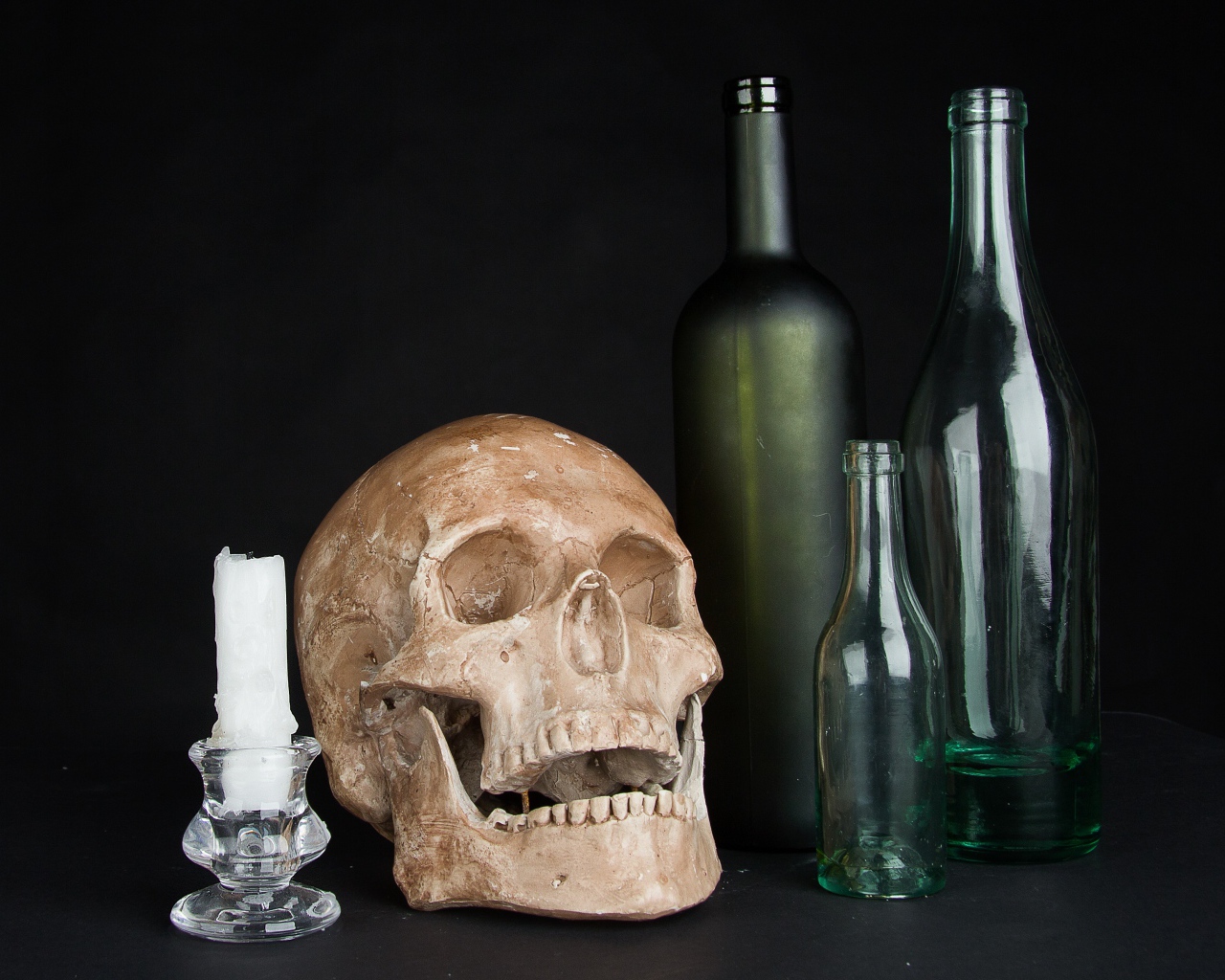 Череп, пустые бутылки и свеча на черном фоне