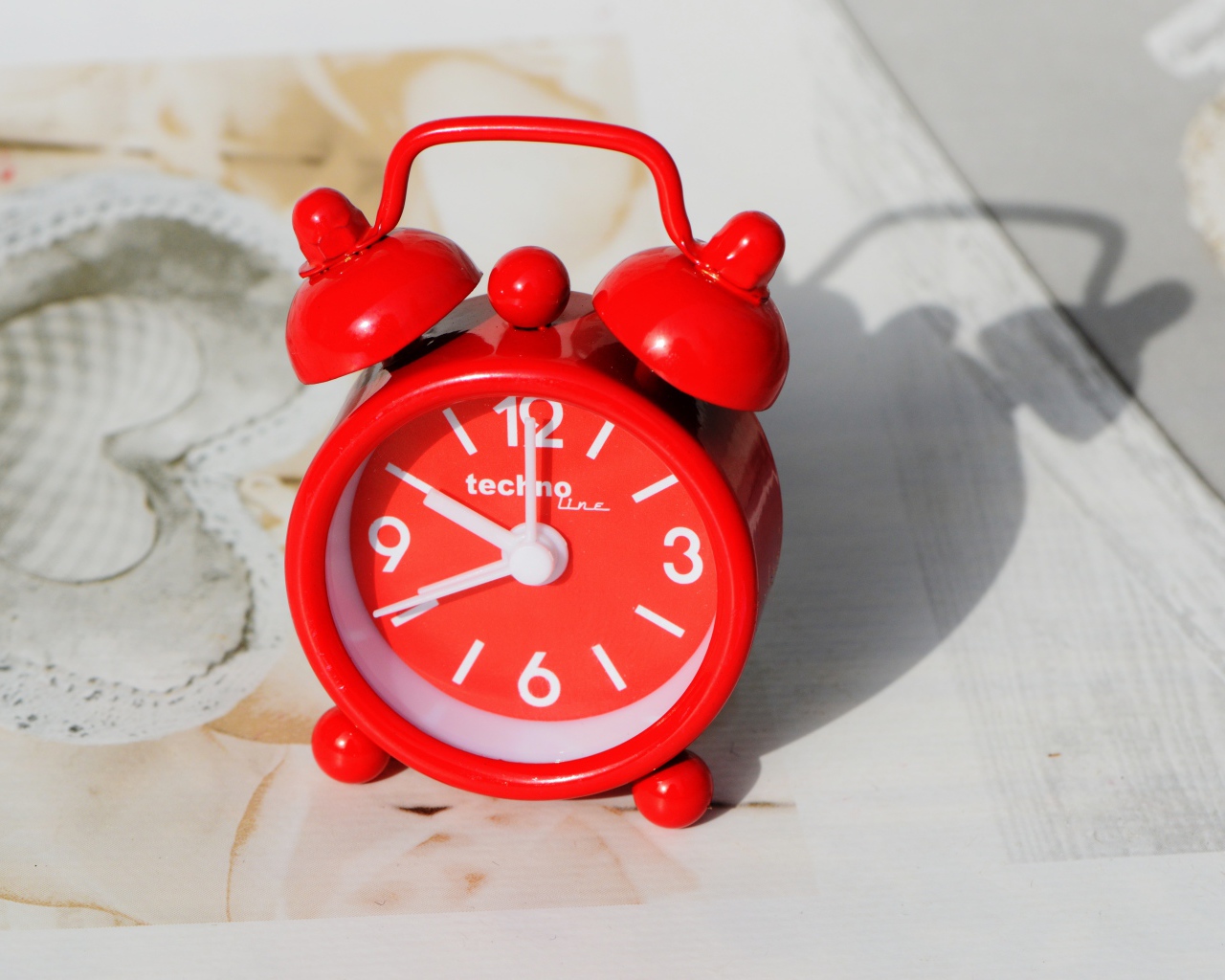 Маленький красный будильник стоит на столе 