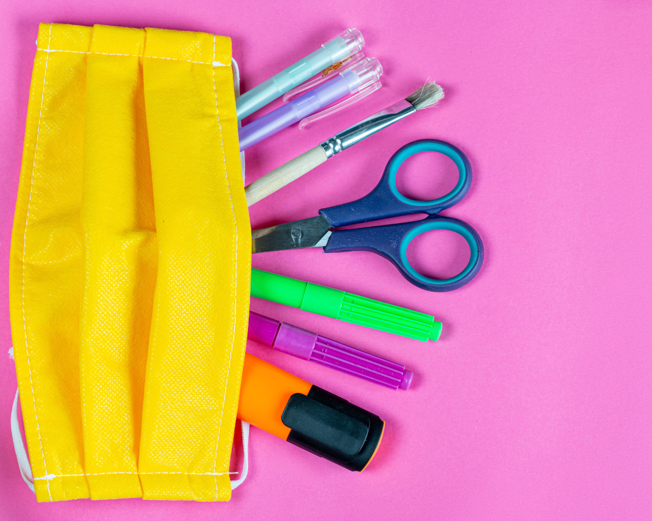 Желтая медицинская маска с ручками и ножницами на  розовом фоне