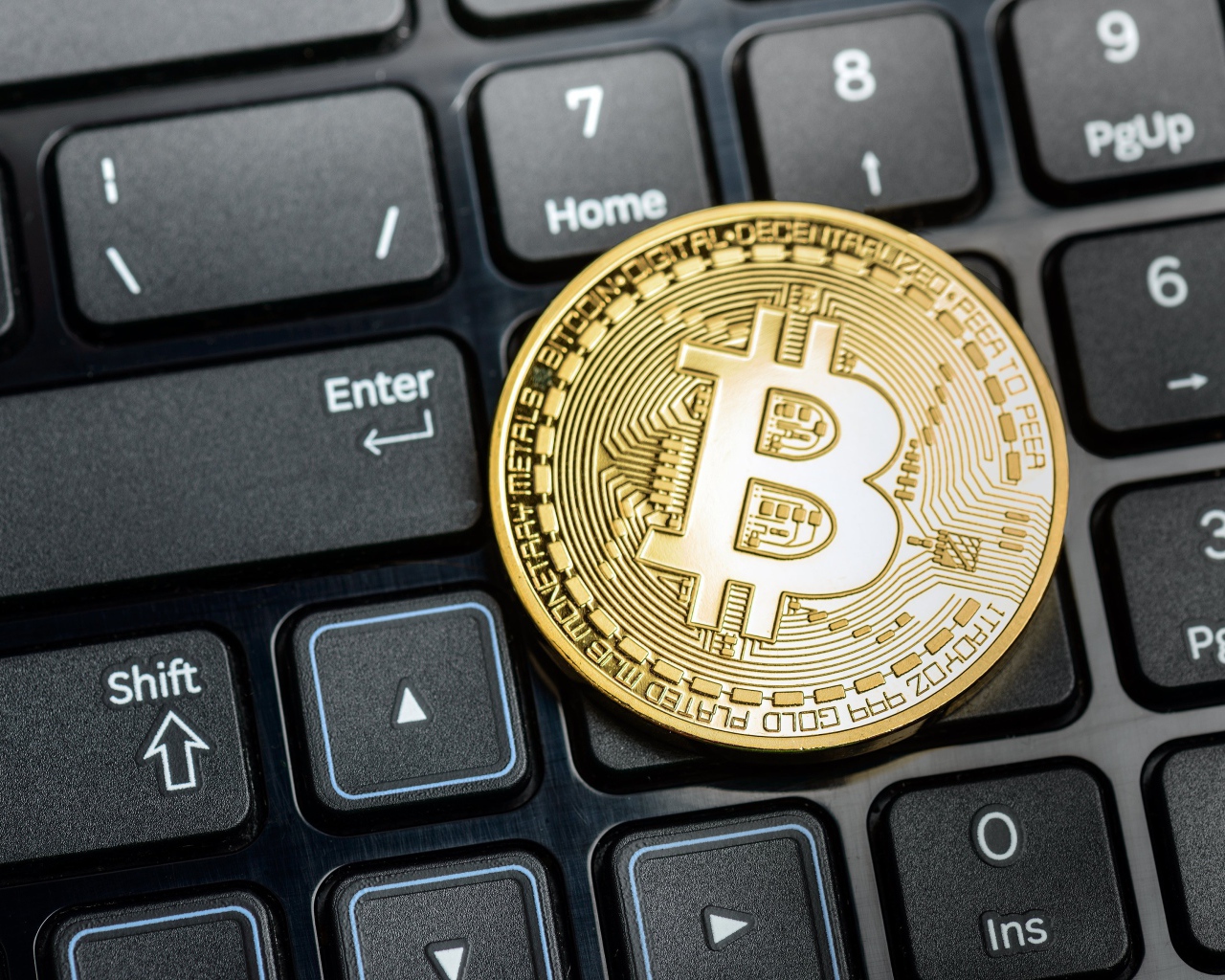 Золотая монета биткоин на черной клавиатуре