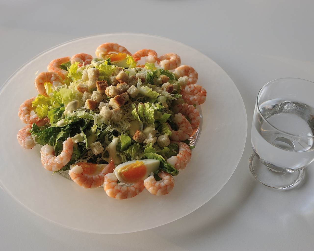 Тарелка аппетитного салата с креветками на столе с рюмкой