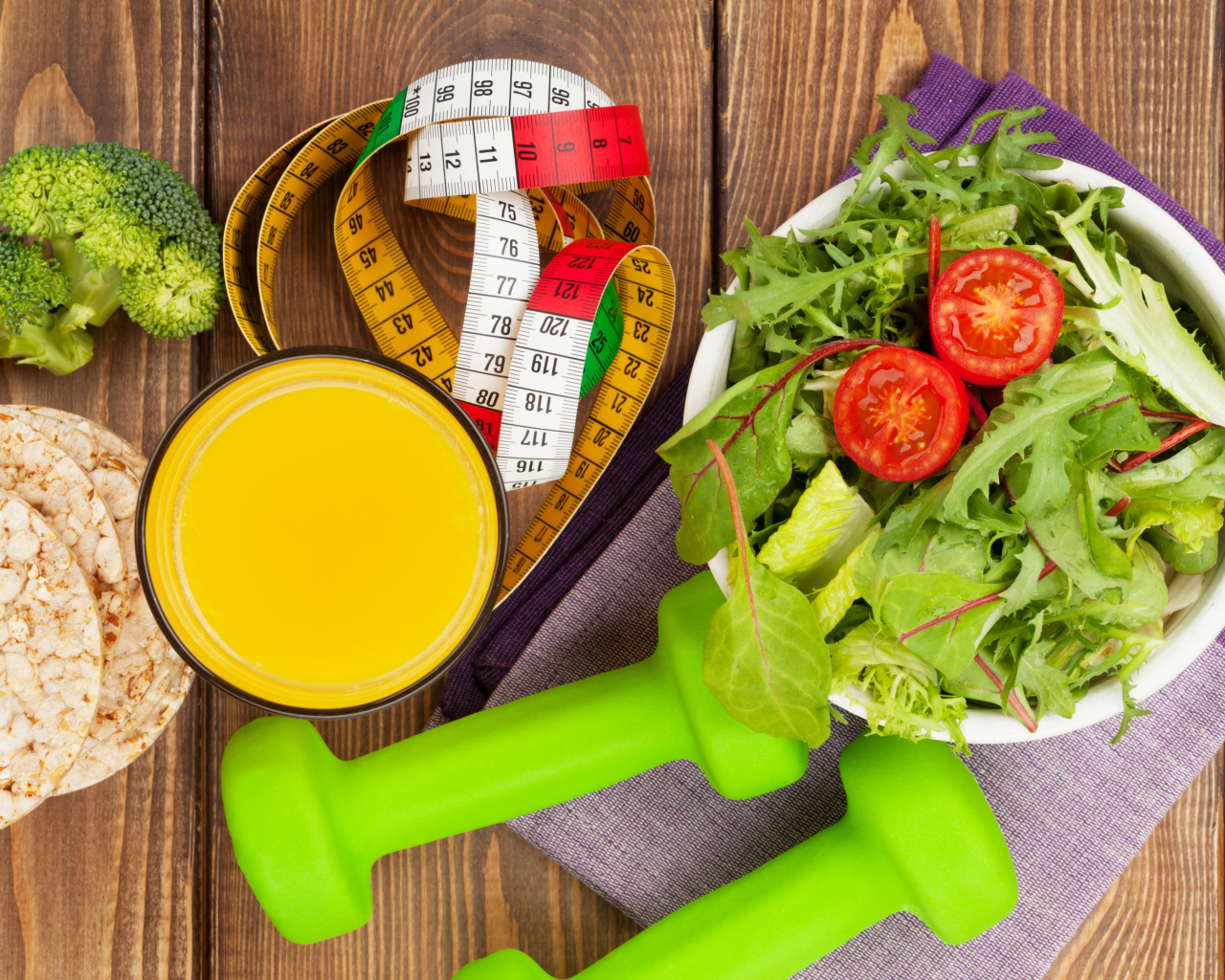 Салат из зелени на столе с соком и гантелями