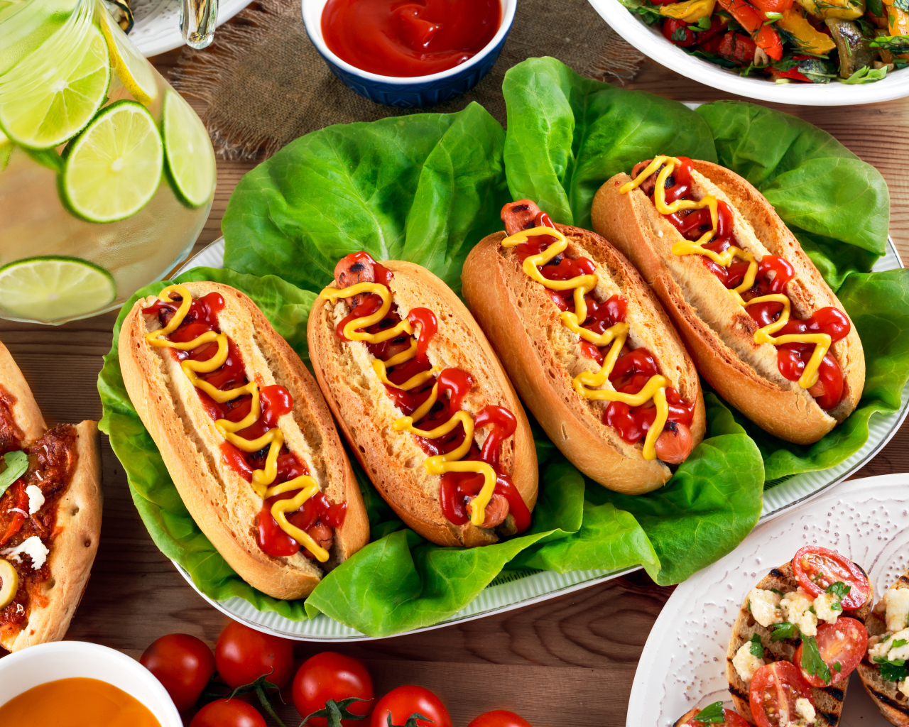 Хотдоги, пицца, лимонад и салат на столе