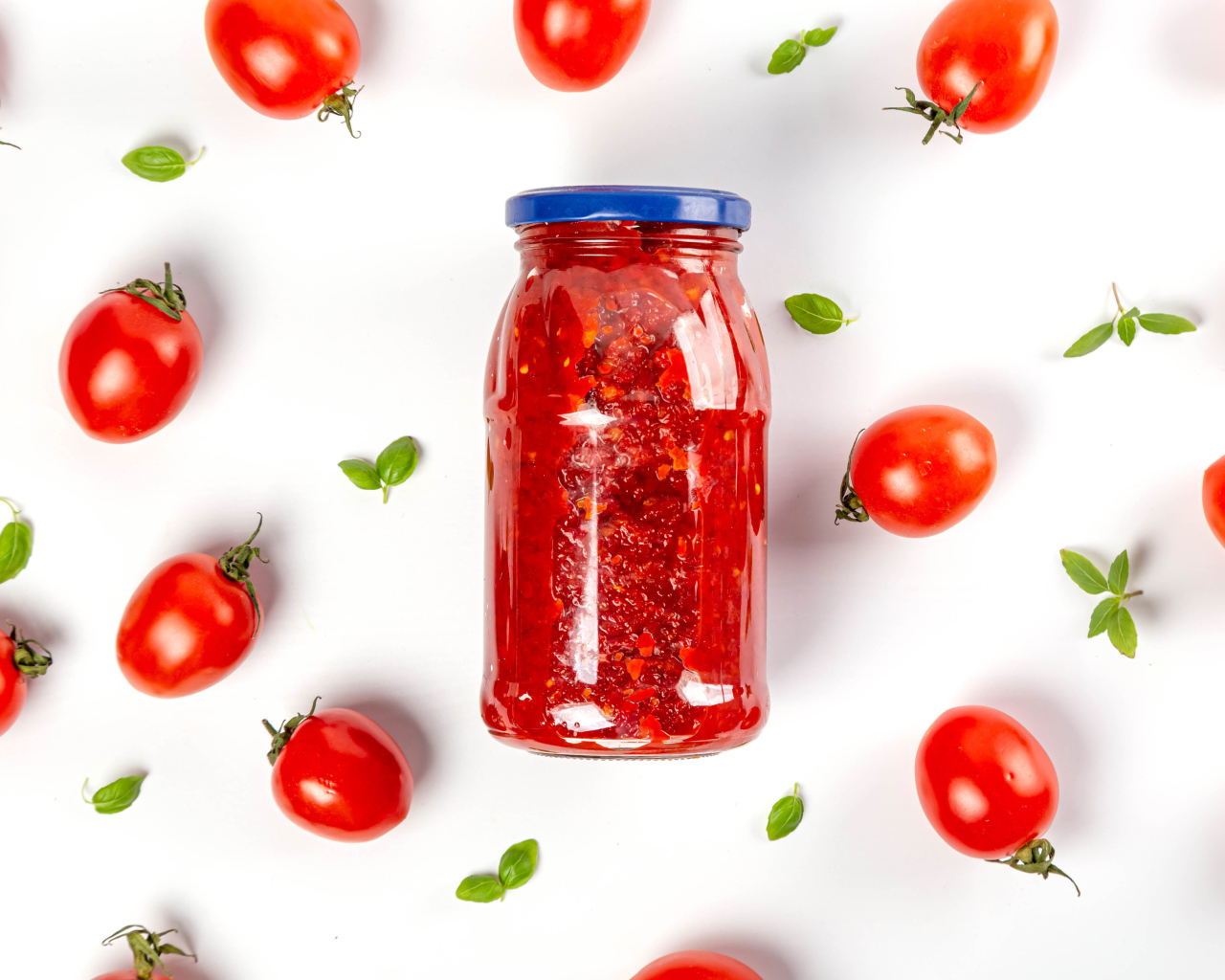 Банка аджики на белом фоне с помидорами