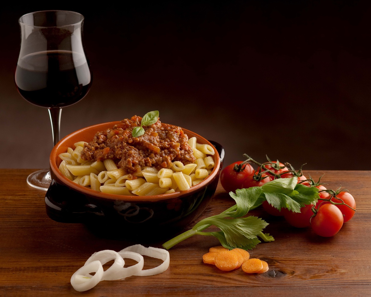 Макароны с фаршем на столе с бокалом вина и помидорами