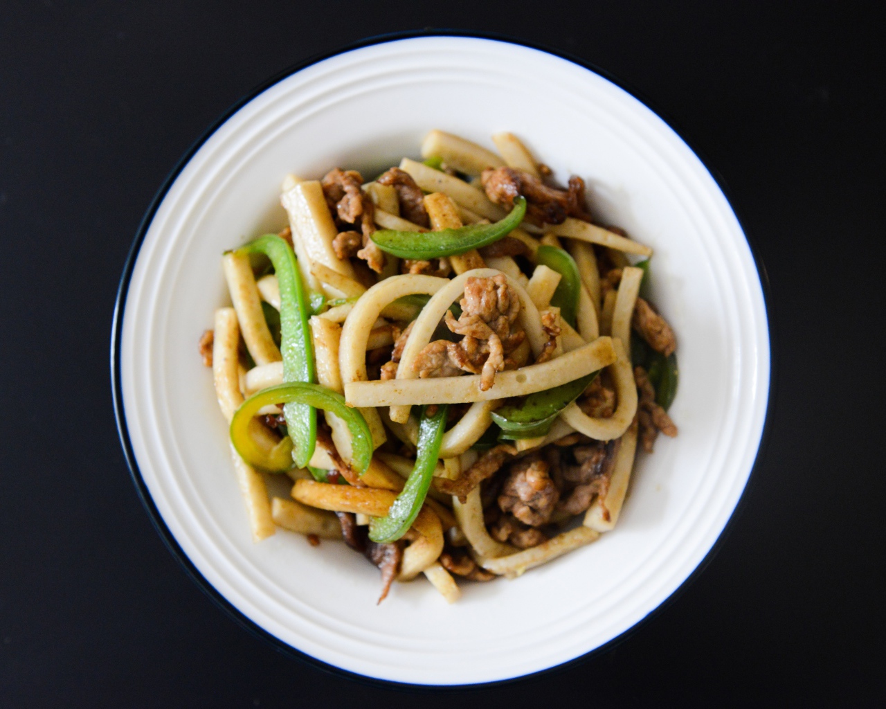 Салат с мясом в белой тарелке на черном фоне