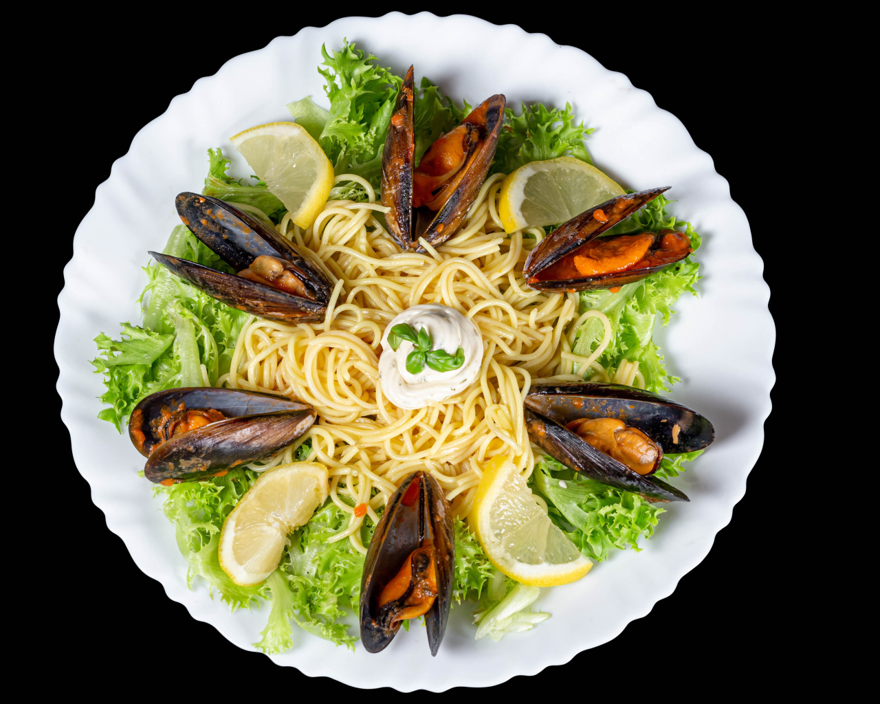 Спагетти с мидиями и листьями салата на белой тарелке