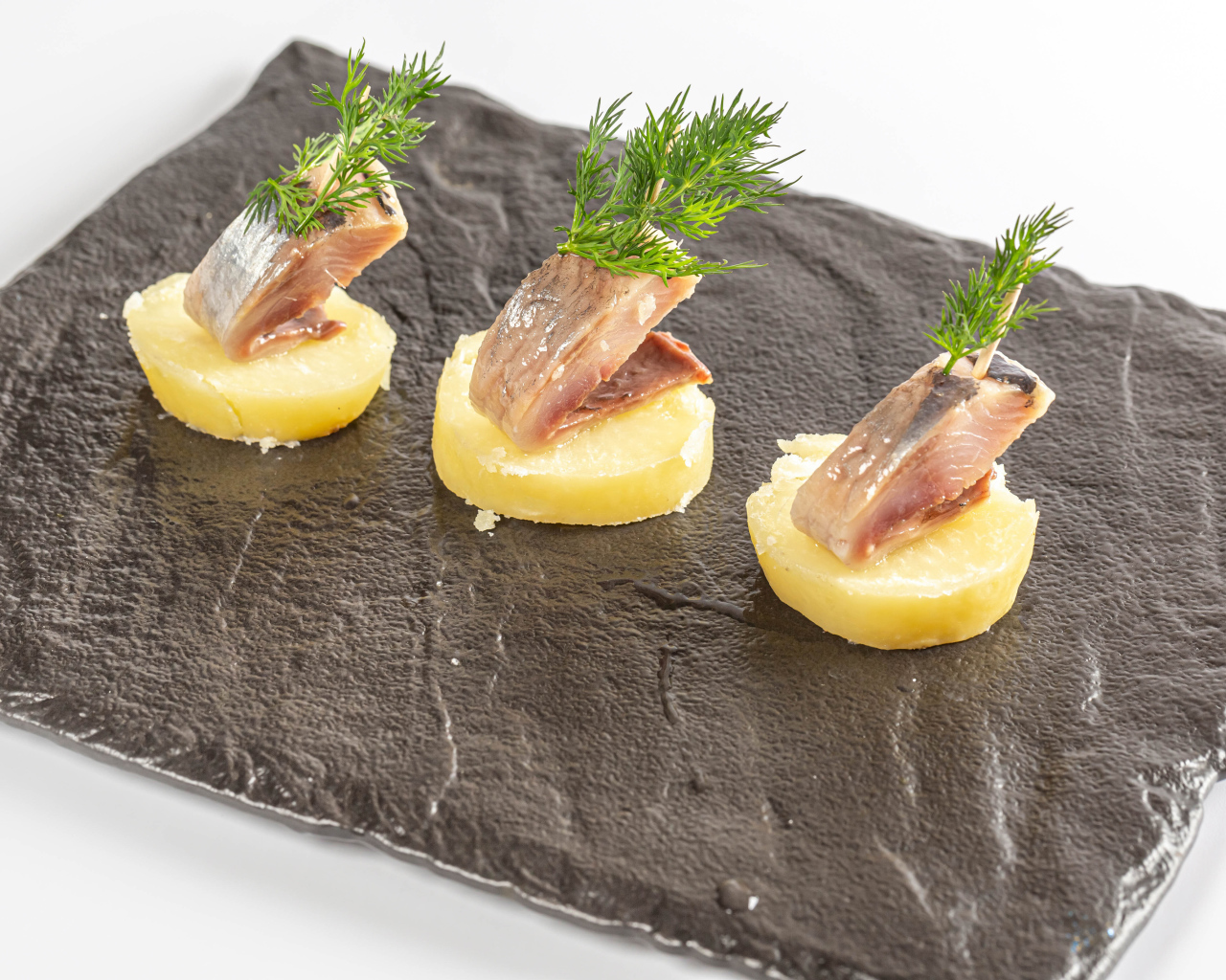 Три куска вареного картофеля с сельдью и укропом