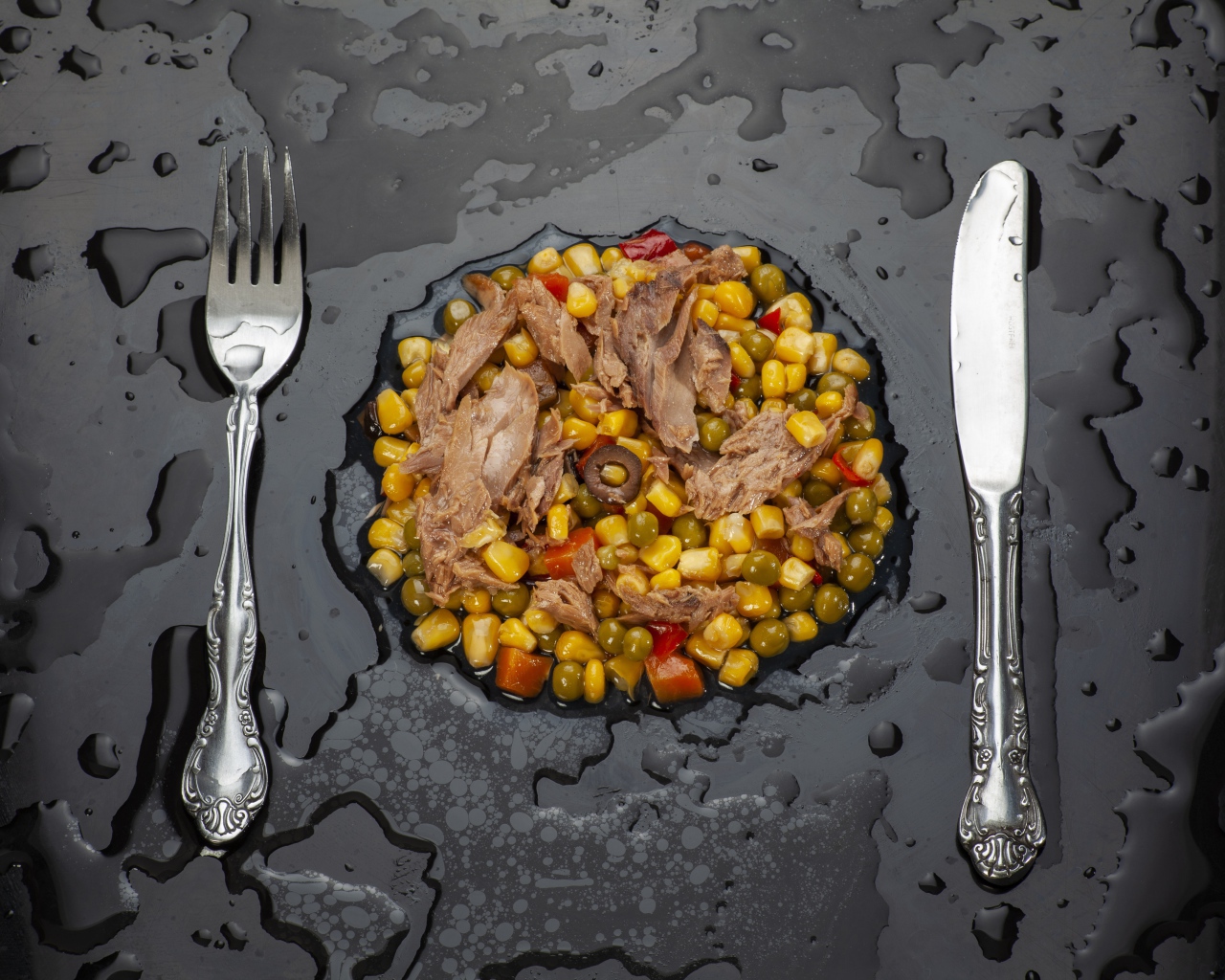 Vegetables with meat and cutlery on a black surface
