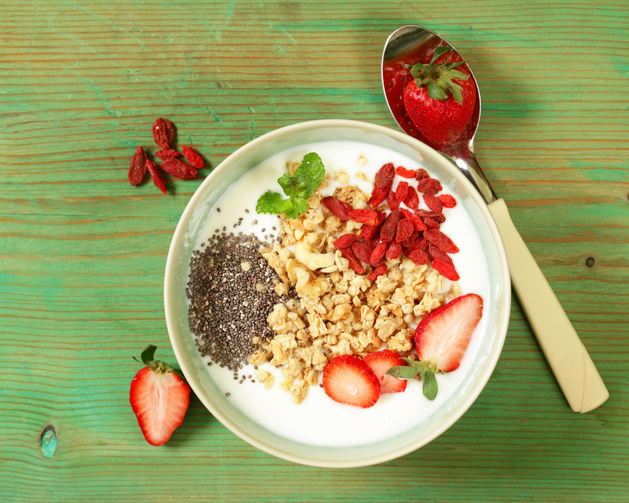 Йогурт с сухофруктами и клубникой на столе в миске 