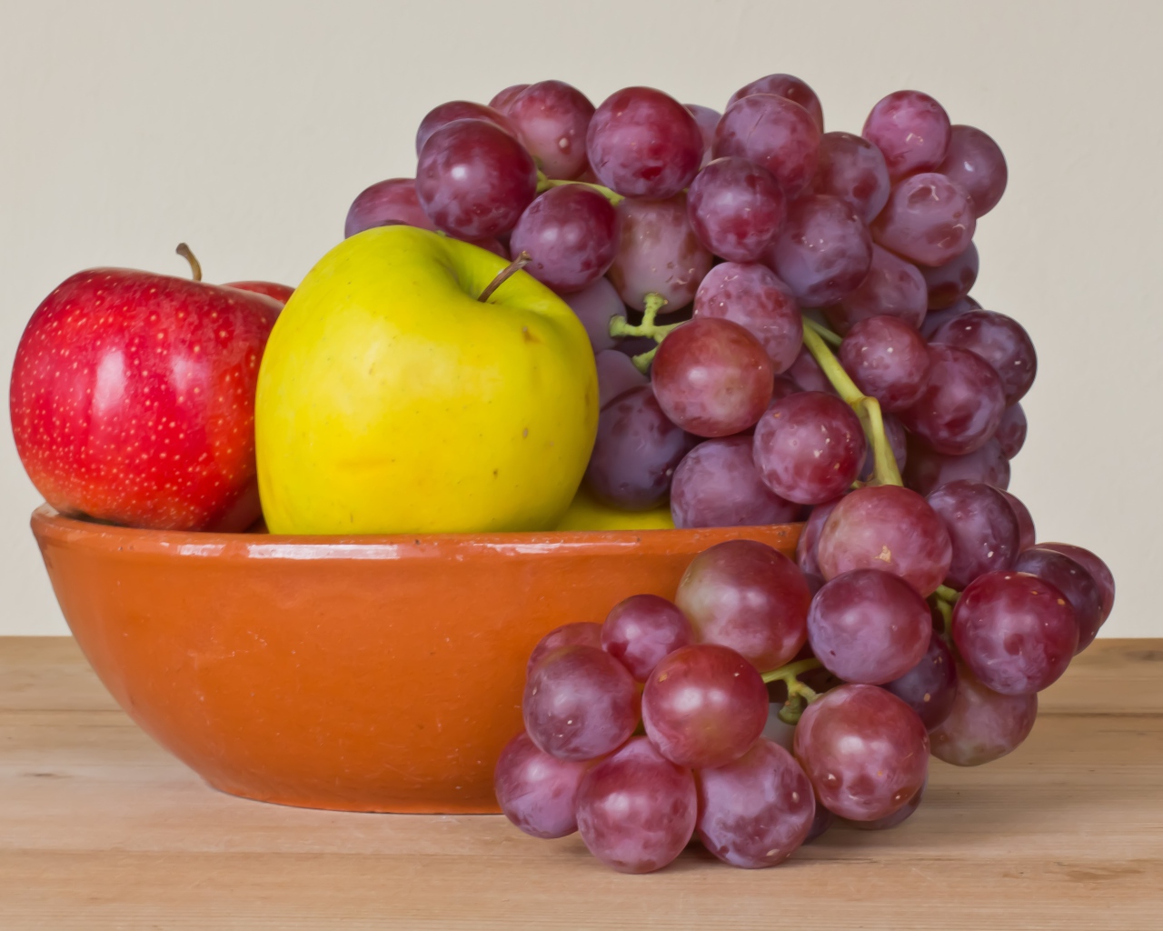 Яблоки и розовый виноград в тарелке на столе 